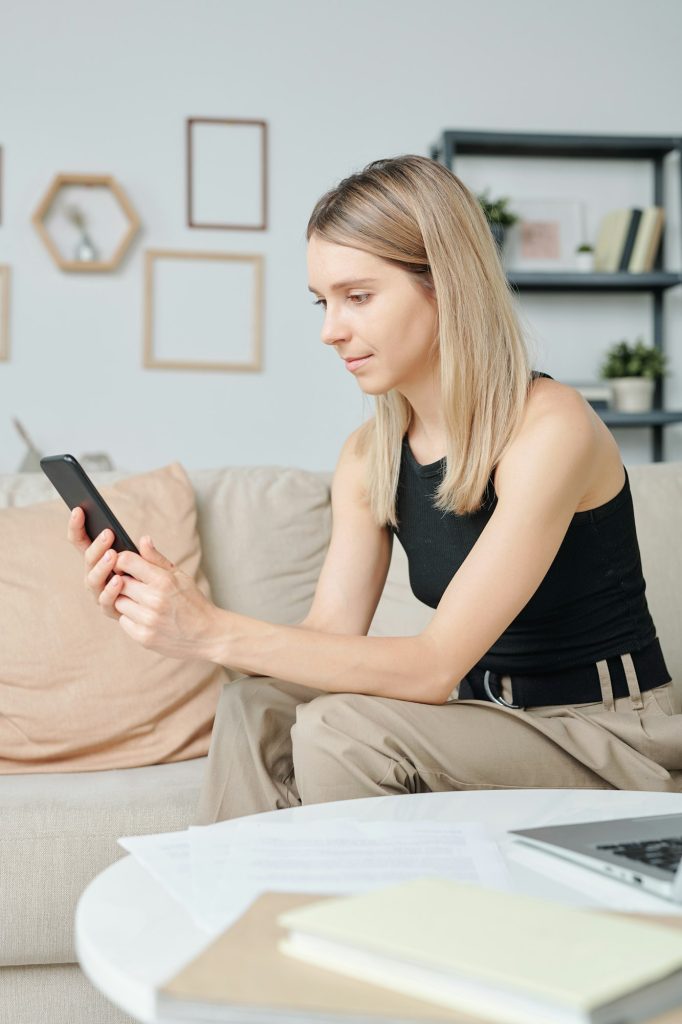 Blond pretty girl in casualwear with smartphone scrolling through contacts